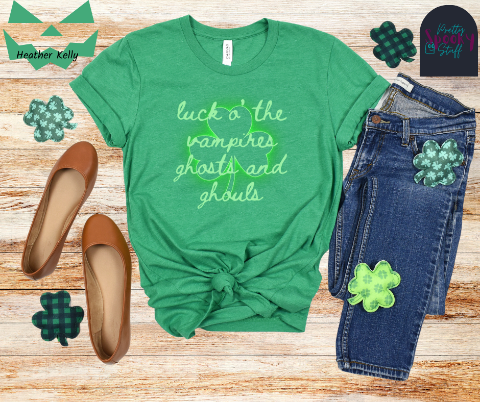 St. Patrick's Day shirt with transparent shamrock that glows green around the edges and the words "luck o' the vampires ghost and ghouls" in cursive light green font over top, in heather kelly.