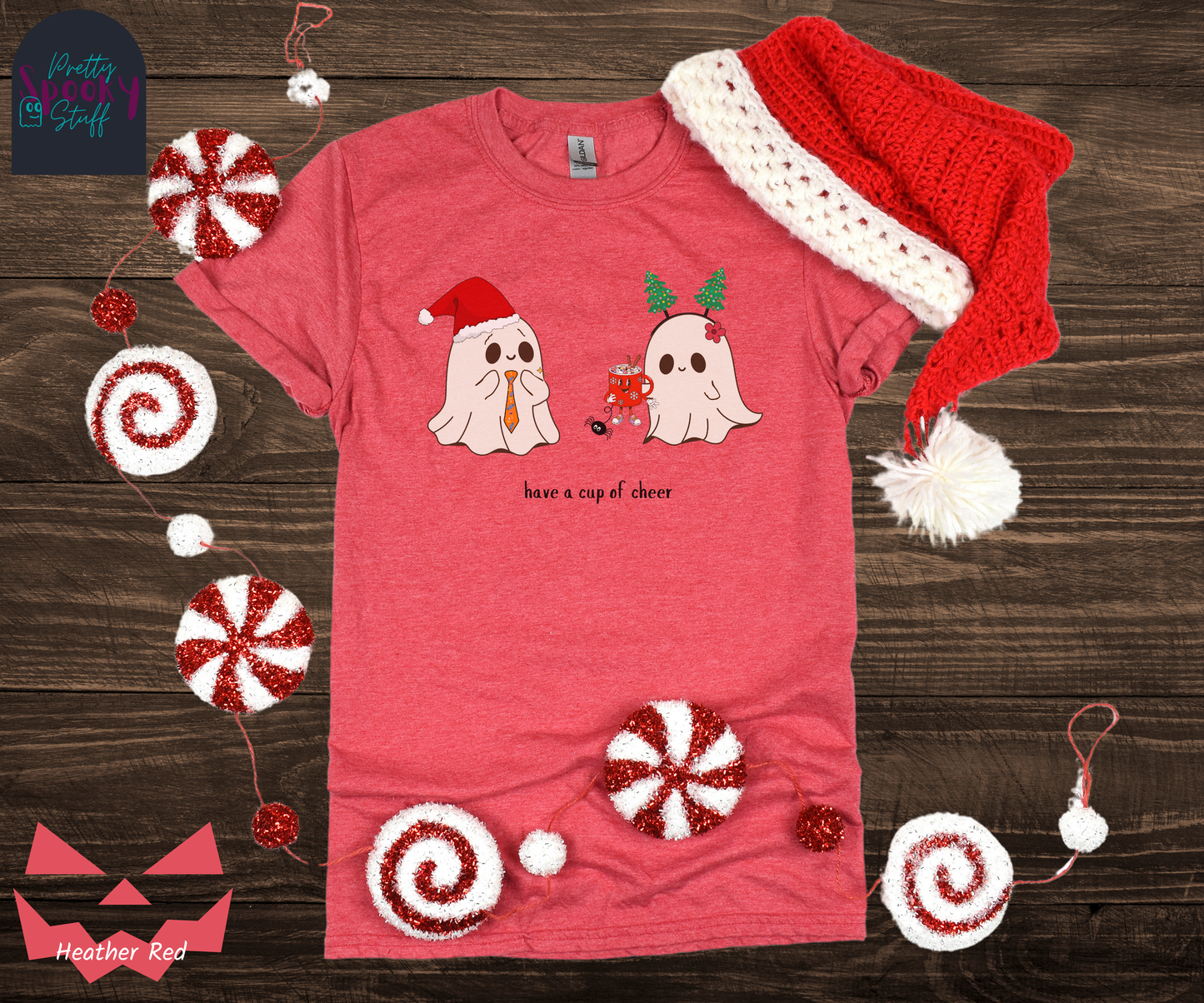 Christmas shirt with two ghosts, one wearing a Santa hat with Halloween candy tie, and one wearing a Christmas tree headband that is handing the other ghost a cup of hot chocolate that has a face and legs, and also a spider hanging from the bottom, with the words "have a cup of cheer" below, in heather red.