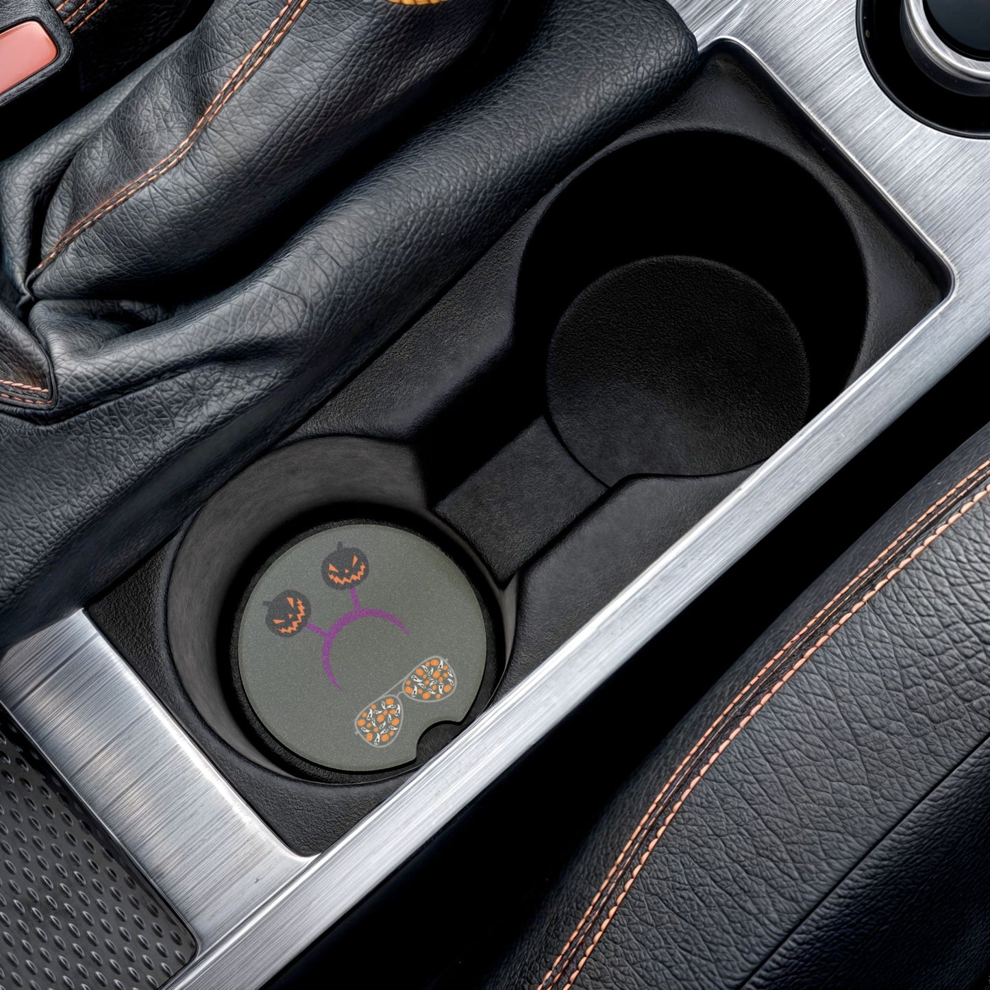 Halloween car coaster with pair of aviator glasses filled with ghosts and pumpkins in the lenses, topped with a purple headband donning dark colored jack o' lanterns, gray background, shown in car cup holder.