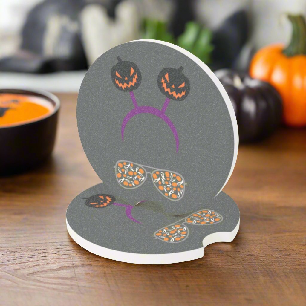 Halloween car coaster with pair of aviator glasses filled with ghosts and pumpkins in the lenses, topped with a purple headband donning dark colored jack o' lanterns, gray background sitting on table.