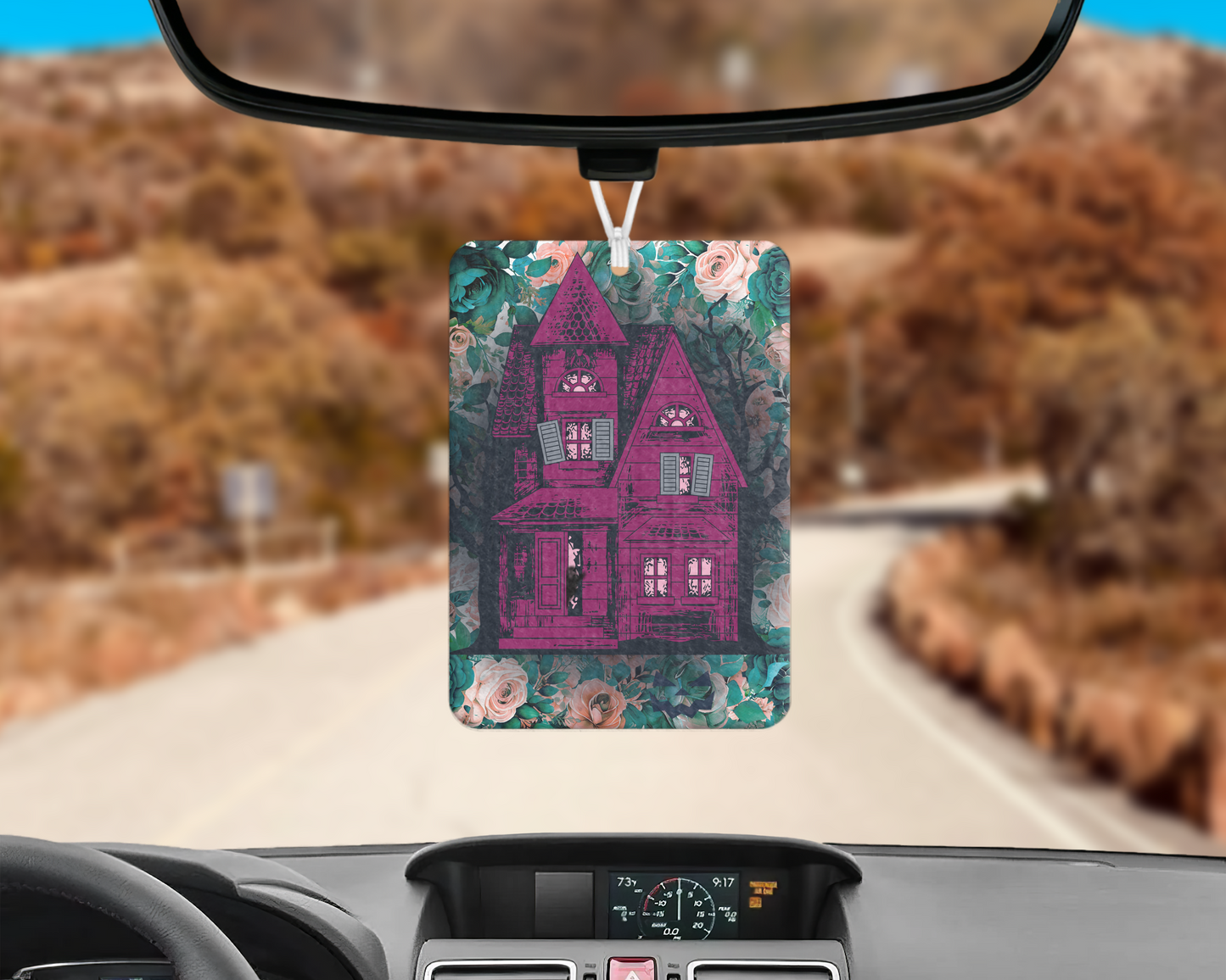 Haunted house Halloween air freshener with purple haunted house sitting on top of a rectangle bed of blue and pink flowers, hanging on rear view mirror.