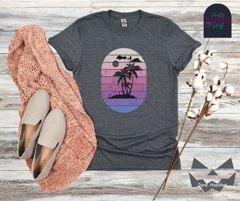 Summerween shirt with oval purple gradient lines, behind small beach and palm trees silhouette, that also has three gravestones on the beach with several ghosts flying above, as well as a witch flying on her broom in the clouds, in dark heather.