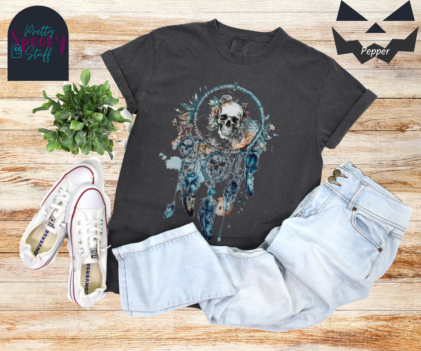 Halloween eerie skull dreamcatcher shirt, watercolor aesthetic in shades of blue, featuring a skull with blue tinted flowers in the main circle, and creepy skull faces hiding amongst the 4 feathers and 2 additional circles hanging below in pepper.