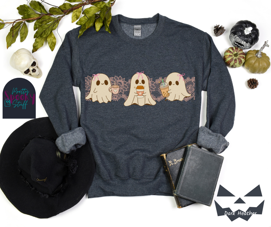 Coquette Halloween sweatshirt with three adorable ghosts, each enjoying their own coffee beverage, adorned with a pink bow, with light pink intricate lace design behind them, in dark heather.