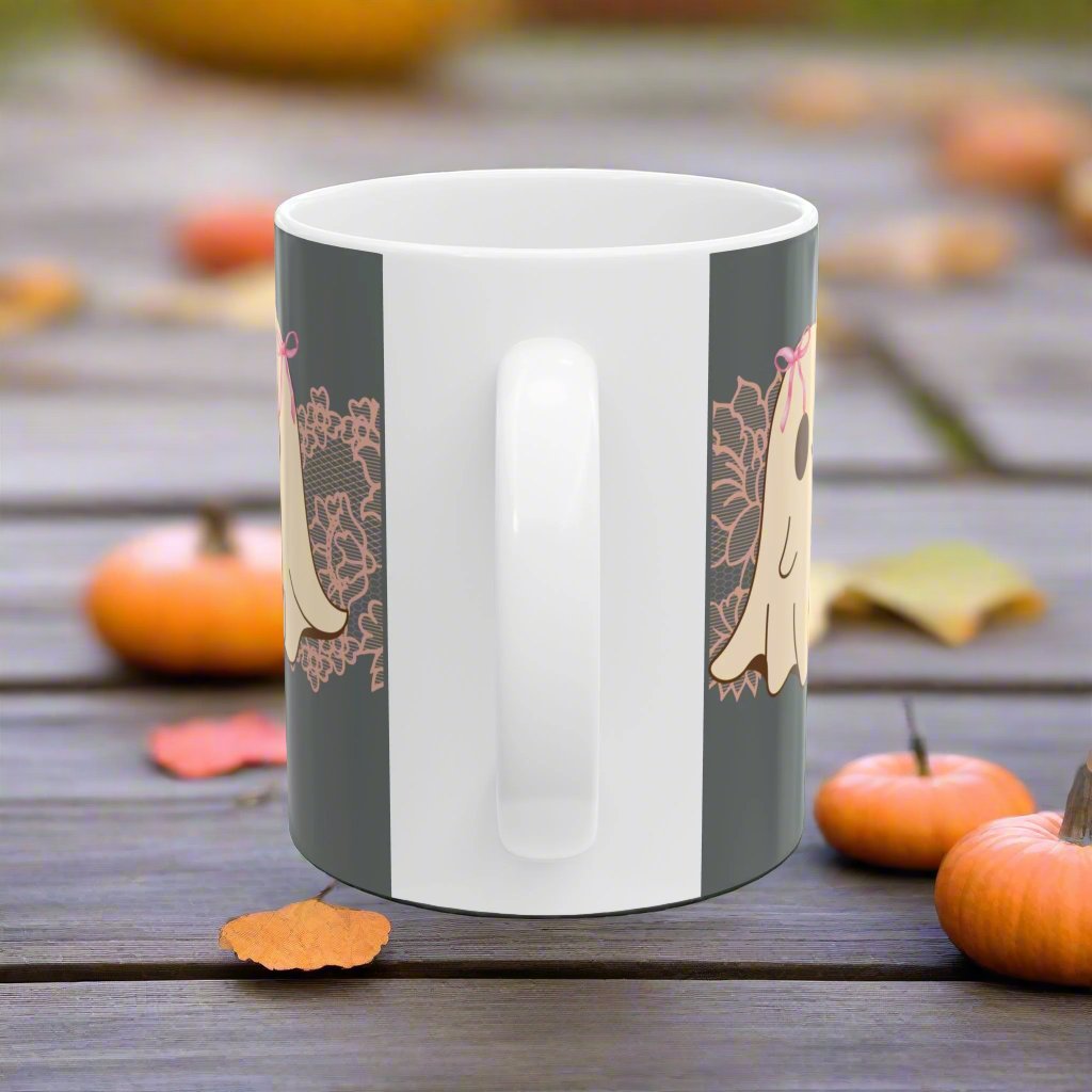 Ceramic Halloween coffee mug with three adorable ghosts, each enjoying their own coffee beverage, adorned with a pink bow, with light pink intricate lace design behind them, gray background, handle view.