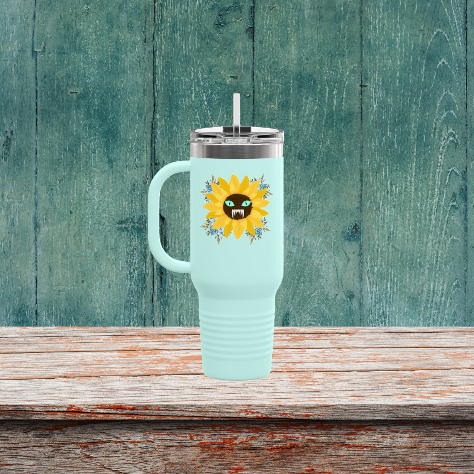 Spooky Girl Summer 40oz tumbler design featuring a sunflower with a menacing face in the middle(striking blue eyes and sharp teeth), with light blue florals in each corner, teal background. Sitting on a wooden table.