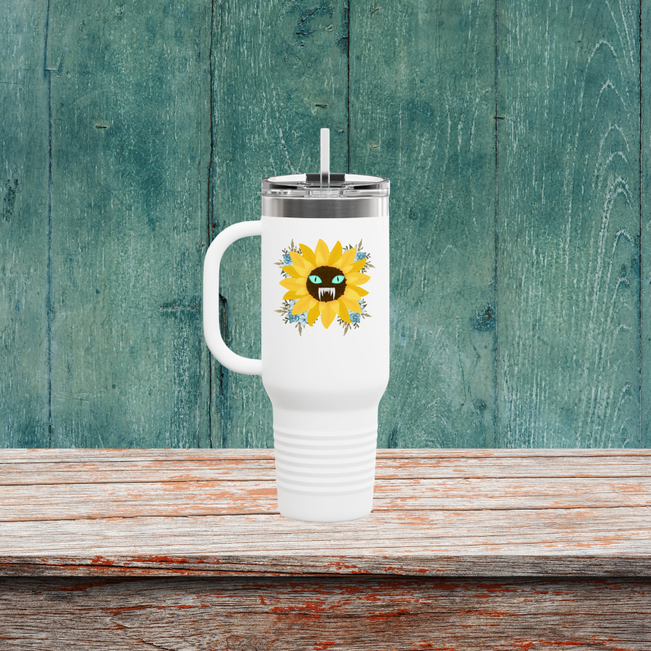 Spooky Girl Summer 40oz tumbler design featuring a sunflower with a menacing face in the middle(striking blue eyes and sharp teeth), with light blue florals in each corner, white background. Sitting on a wooden table.