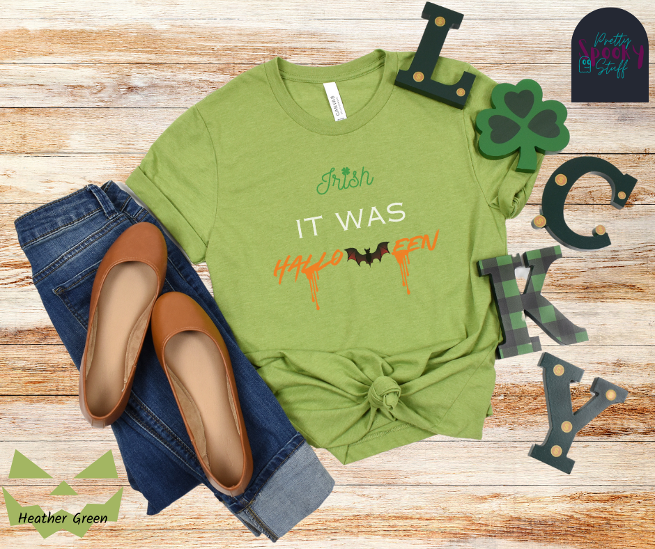 St. Patrick's Day shirt with the word "Irish" in green and a clover for the "I" dot, the words "it was" in white all uppercase, and "Halloween" in orange with a bat in place of the "w" and orange blood drips off two letters, in heather green.
