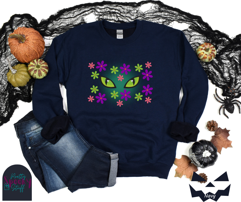 Cat Halloween sweatshirt with spooky green cat eyes in the middle of purple, pink and green flowers, with a blue glow behind them, in navy.
