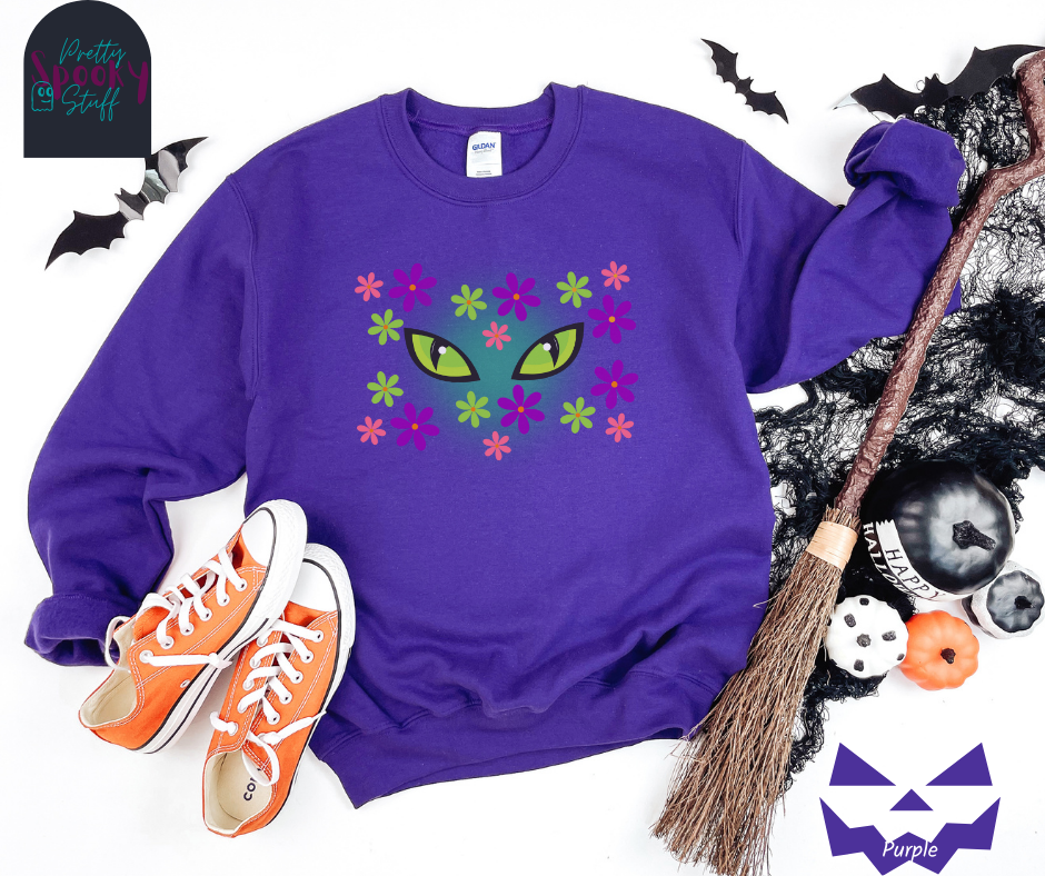 Cat Halloween sweatshirt with spooky green cat eyes in the middle of purple, pink and green flowers, with a blue glow behind them, in purple.