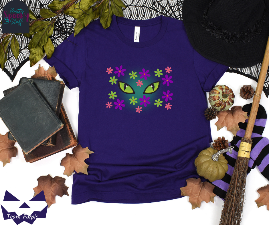 Black cat Halloween shirt with bright green cat eyes in the midst of pink, green, and purple flowers with a blue glow behind them, in team purple.