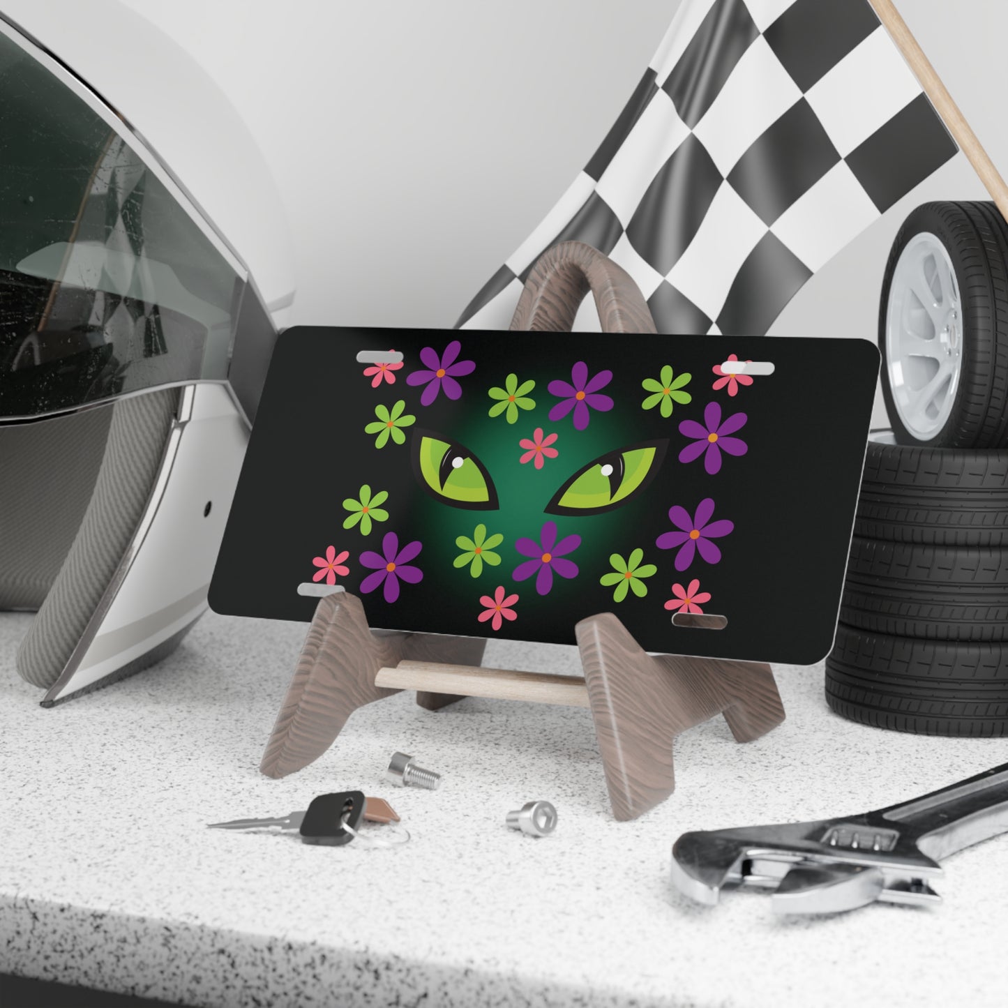 Cat Halloween vanity plate with spooky green cat eyes in the middle of purple, pink and green flowers, with a blue glow behind them, black background sitting on stand.