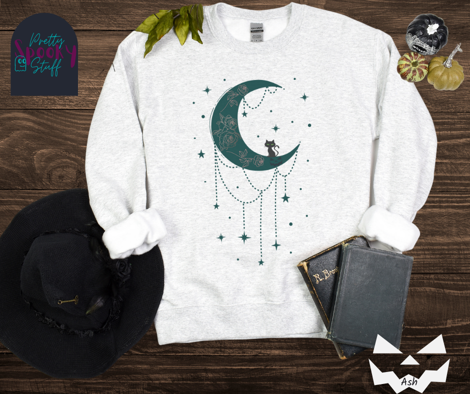 Moon and stars Halloween sweatshirt with a teal crescent moon with pink floral design inside of it, beads hanging from the bottom, a black cat perched on the bottom, and teal stars surrounding it, in ash.