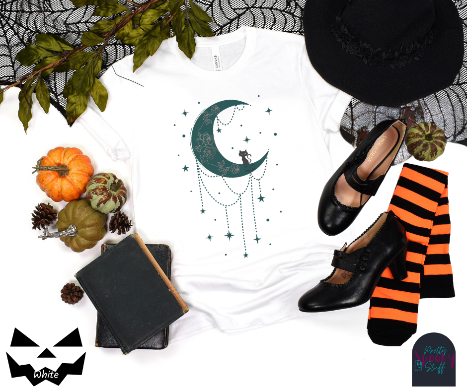Moon and stars Halloween shirt with a teal crescent moon with pink floral design inside of it, beads hanging from the bottom, a black cat perched on the bottom, and teal stars surrounding it, in white.