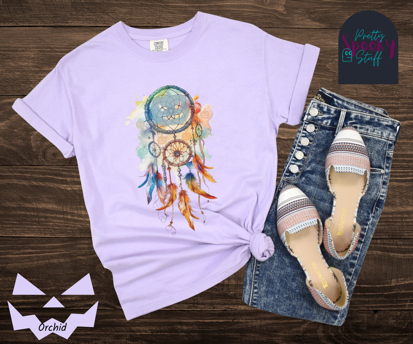 Halloween pumpkin dream catcher shirt, watercolor aesthetic in rusts, peaches, and light blues, with three small circles and 6 feathers hanging from the main circle that features a light blue jack o' lantern silhouette, several more jack o' lanterns hide amongst the colors, in orchid.