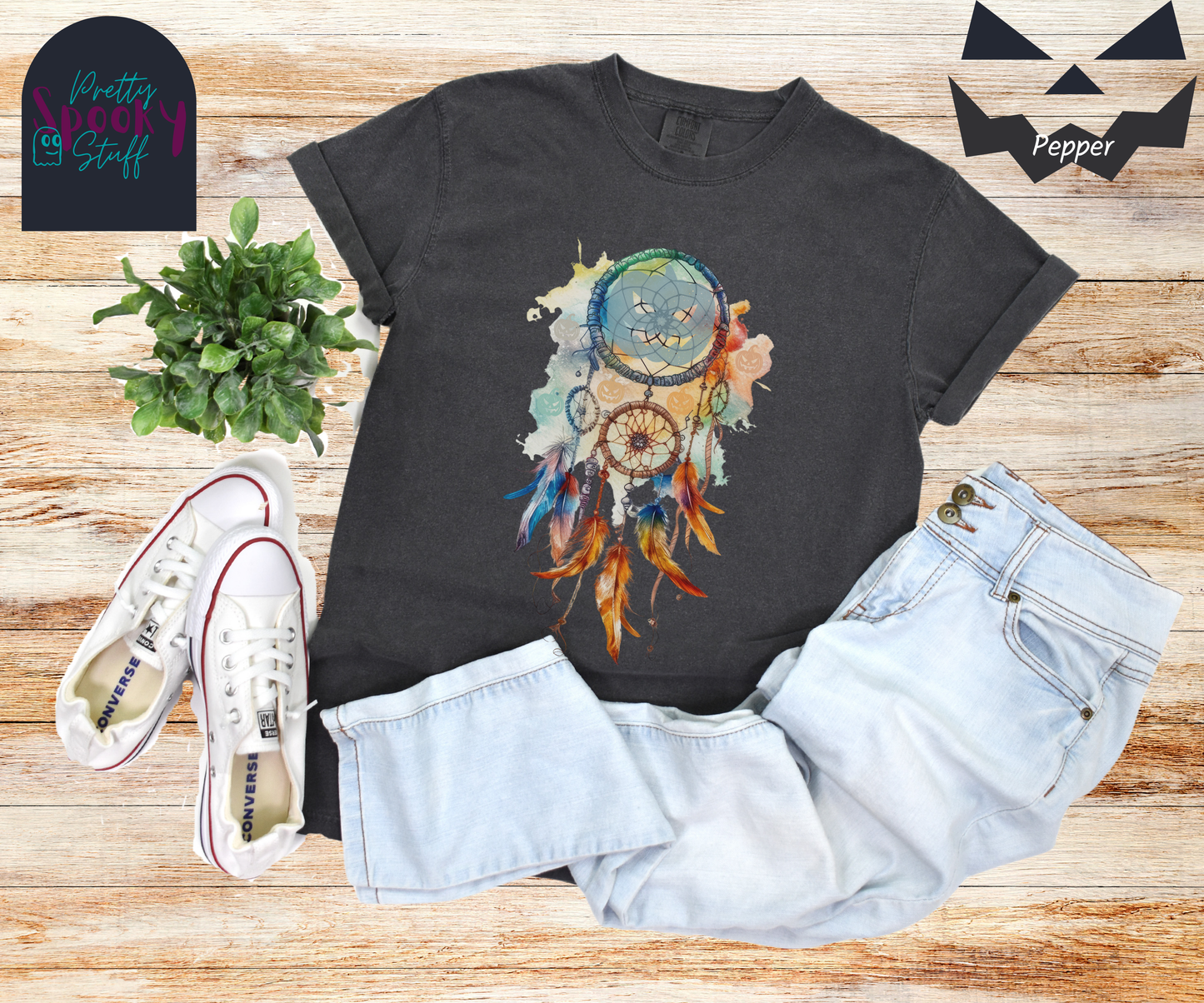 Halloween pumpkin dream catcher shirt, watercolor aesthetic in rusts, peaches, and light blues, with three small circles and 6 feathers hanging from the main circle that features a light blue jack o' lantern silhouette, several more jack o' lanterns hide amongst the colors, in pepper.
