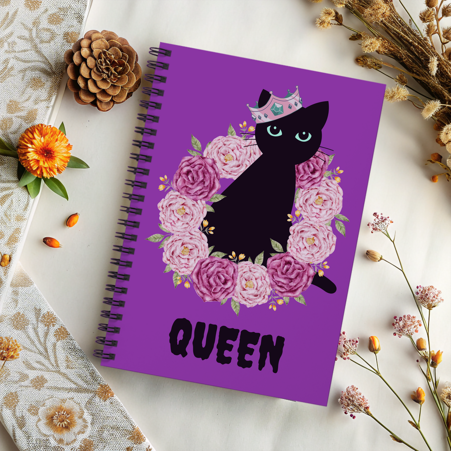 Spooky Girl Summer spiral notebook featuring black cat sitting in ring of pink and purple roses, wearing a crooker crown with the word "queen" below in black, with purple background.