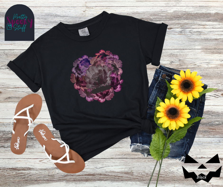 Summerween shirt with flowers of different shades of purple arranged in the shape of a heart, with shadows of running zombies and two zombie arm line drawings mixed in, in black.