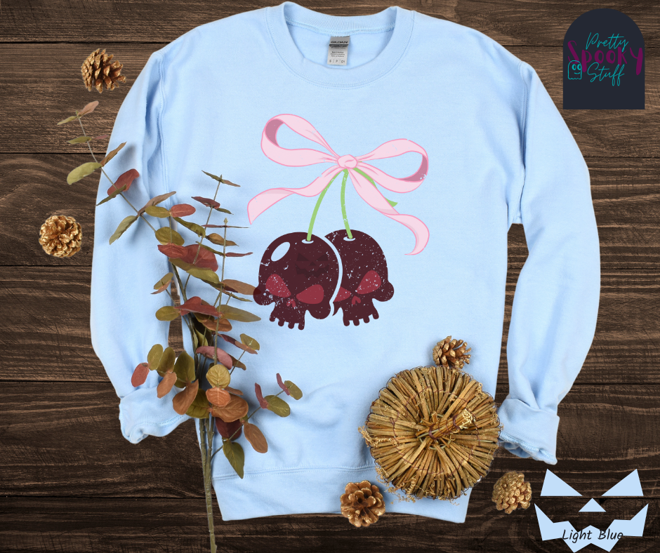 Coquette Halloween sweatshirt with two skull shaped cherries tied together with a large light pink bow, vintage style, in light blue.