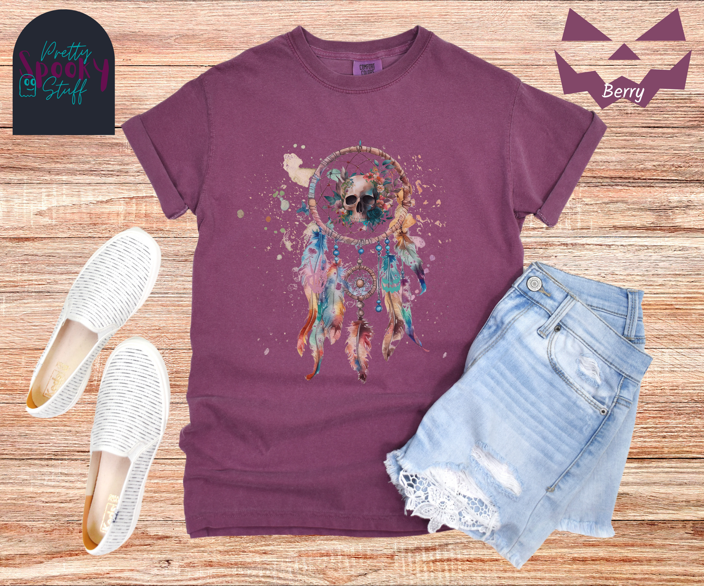 Halloween skull dream catcher shirt, watercolor aesthetic in pinks, blues, and purples, featuring a creepy skull with flowers behind it in the main circle, and skeleton hand and jack o lantern face hidden amongst the 5 feathers hanging below, in berry.
