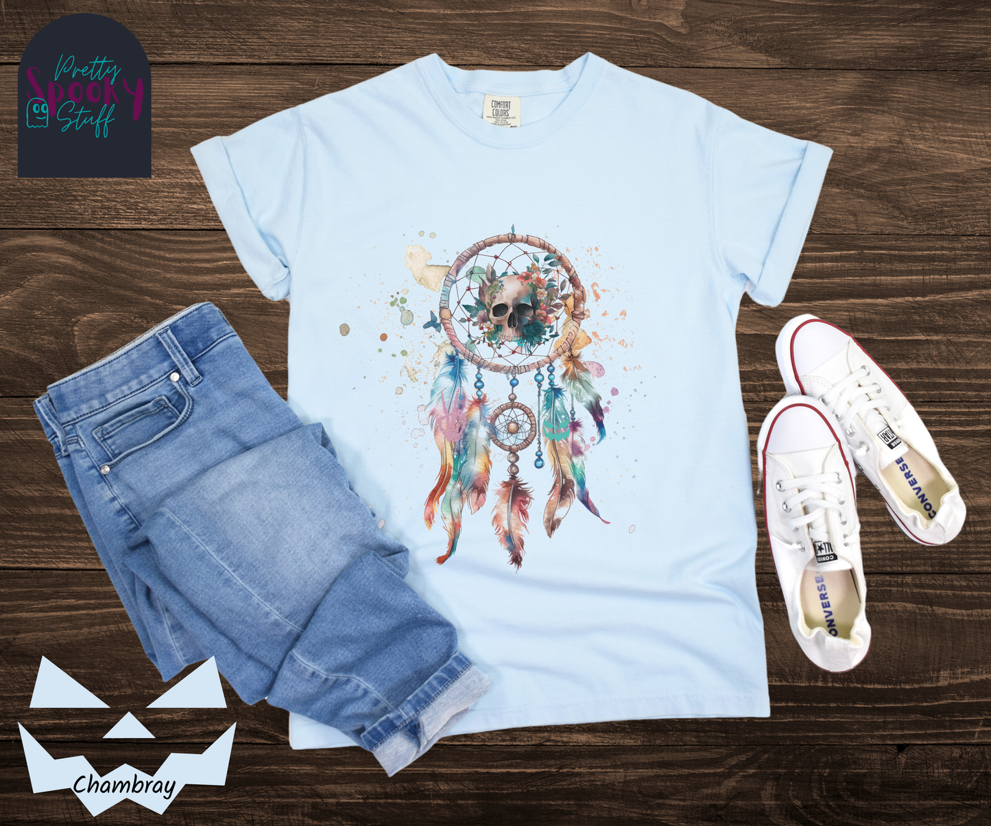 Halloween skull dream catcher shirt, watercolor aesthetic in pinks, blues, and purples, featuring a creepy skull with flowers behind it in the main circle, and skeleton hand and jack o lantern face hidden amongst the 5 feathers hanging below, in chambray.