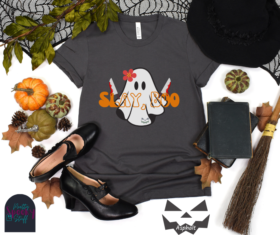 Ghost Halloween shirt with a ghost wearing pink flower, holding two bloody butcher knives and the words "slay boo" in orangle font in front of her, in asphalt.