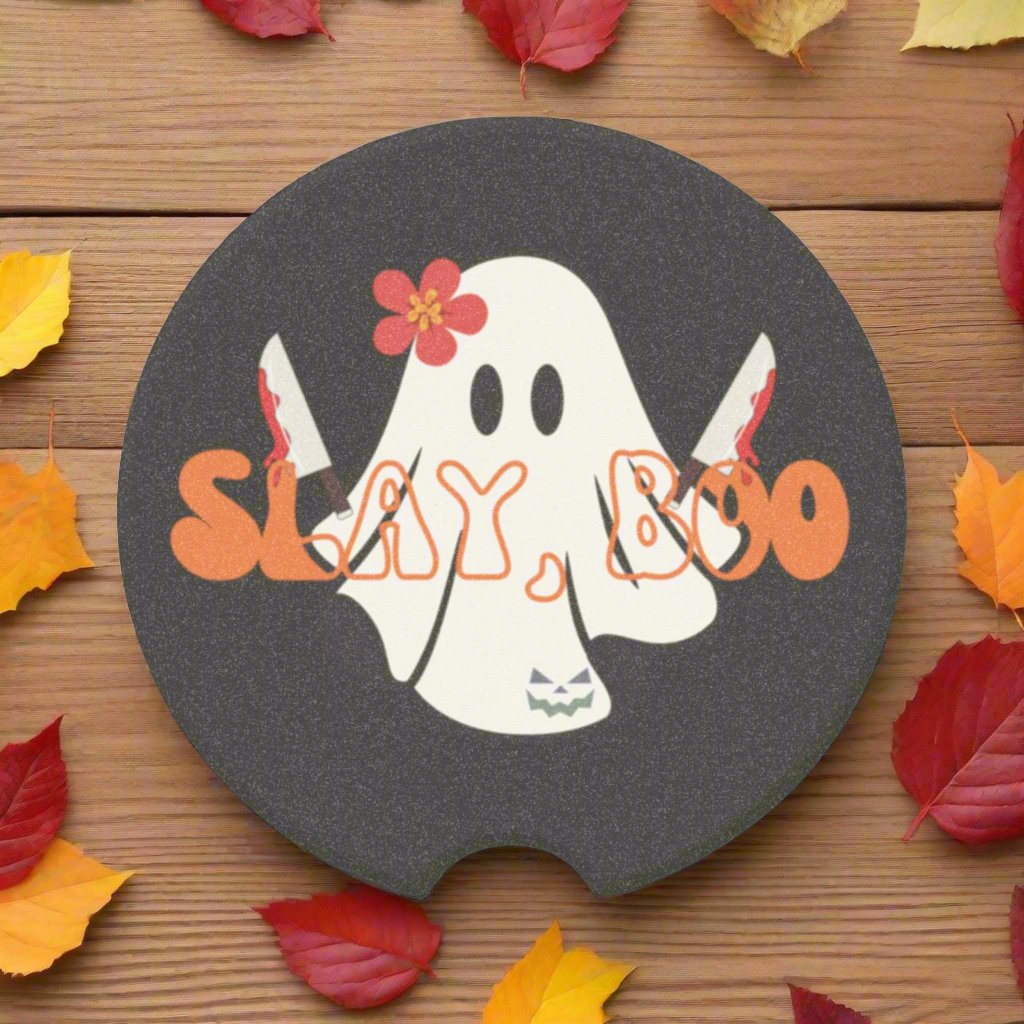 Halloween car coaster with a ghost wearing a pink flower, holding two bloody knives with the words "slay boo" in orange vintage font in front, black background.