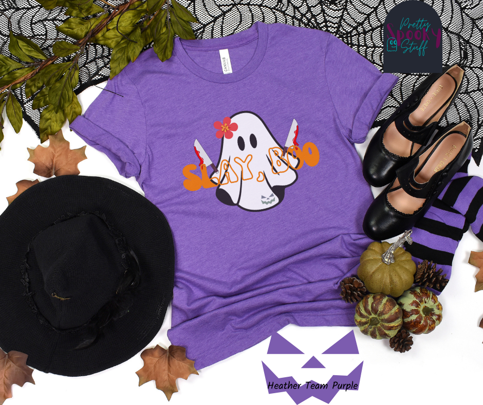 Ghost Halloween shirt with a ghost wearing pink flower, holding two bloody butcher knives and the words "slay boo" in orangle font in front of her, in heather team purple.