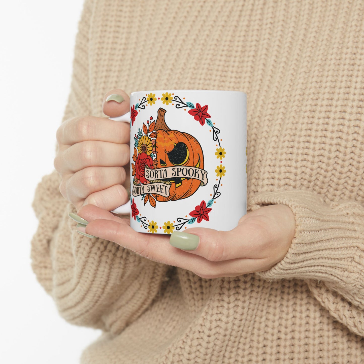 Halloween mug with a circle of yellow, red, and blue flowers, surrounding a half jack o' lantern half floral design with the words "sorta sweet sorta spooky" on small banners across the front, being held by hands.