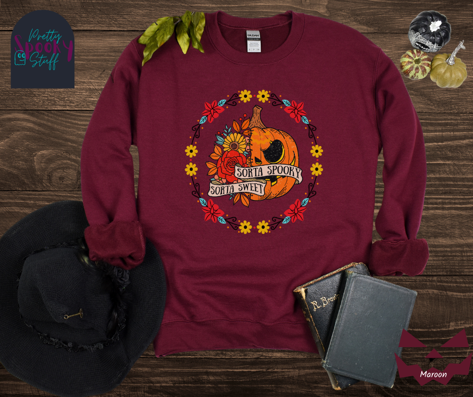 Halloween sweatshirt with a circle of yellow, red, and blue flowers, surrounding a half jack o'lantern half floral design with the words "sorta sweet sorta spooky" on banners, in maroon.