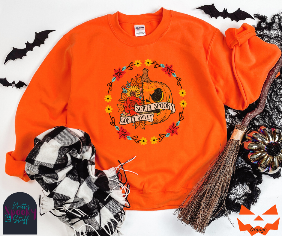 Halloween sweatshirt with a circle of yellow, red, and blue flowers, surrounding a half jack o'lantern half floral design with the words "sorta sweet sorta spooky" on banners, in orange.