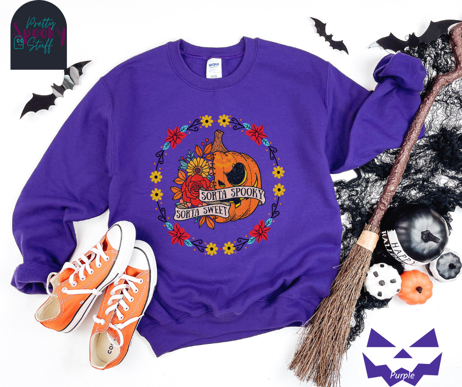 Halloween sweatshirt with a circle of yellow, red, and blue flowers, surrounding a half jack o'lantern half floral design with the words "sorta sweet sorta spooky" on banners, in purple.