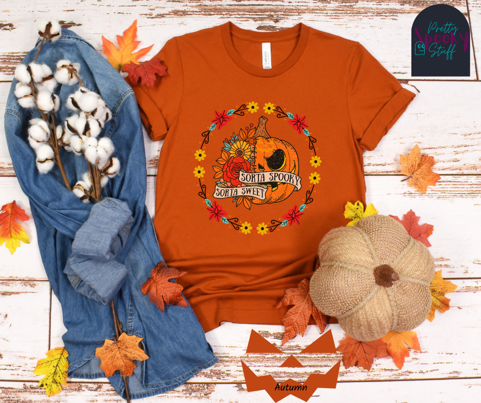 Pumpkin Halloween shirt with a circle of yellow, red, and blue flowers, surrounding a half jack o' lantern half floral design with the words "sorta sweet sorta spooky" on banners, in autumn.