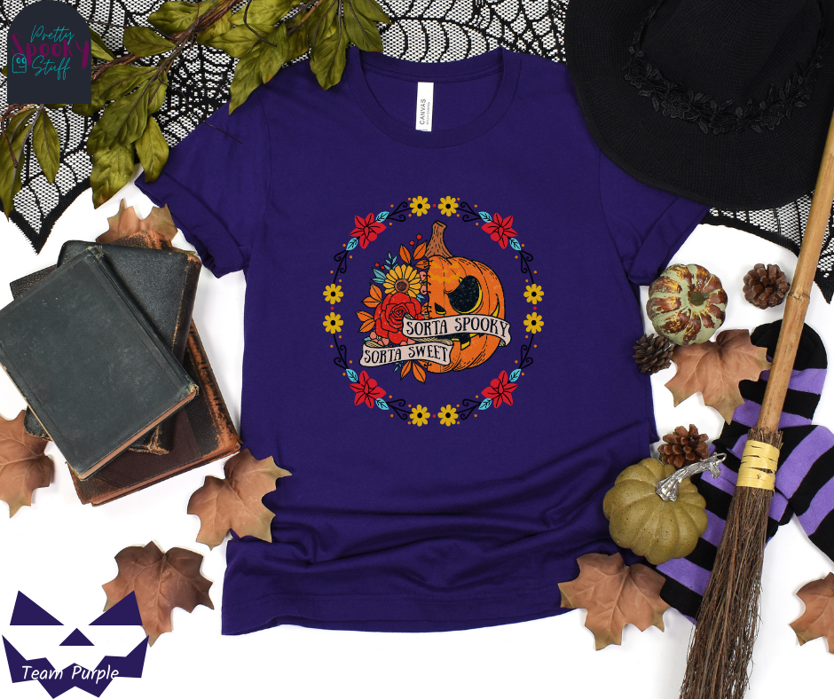 Pumpkin Halloween shirt with a circle of yellow, red, and blue flowers, surrounding a half jack o' lantern half floral design with the words "sorta sweet sorta spooky" on banners, in team purple.