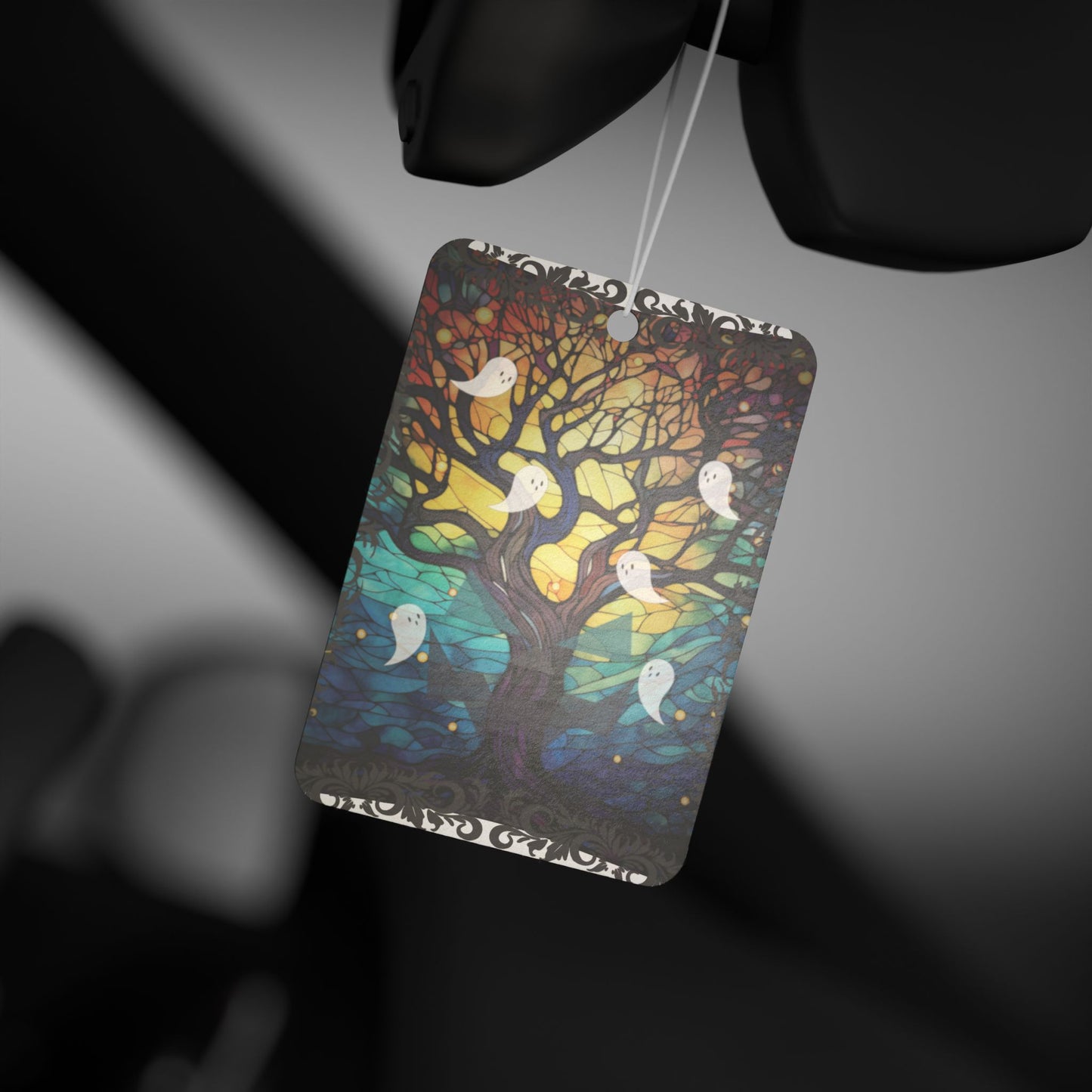 Halloween ghosts air freshener with stained glass design featuring a sprawling bare tree reaching upwards and ghosts flying all around, hanging from rear view mirror.