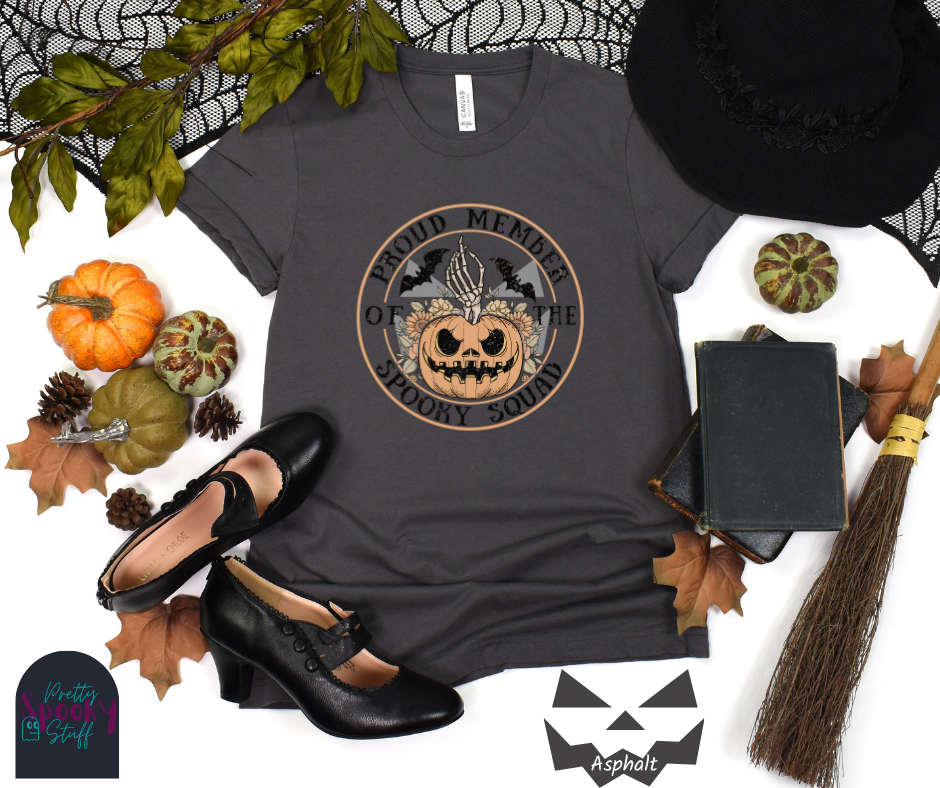 Pumpkin Halloween shirt with jack o' lantern in front of sunflowers, a skeleton hand popping out the top, two bats above, and the words "proud member of the spooky squad" making a circle around it all, faded vintage look, in asphalt.