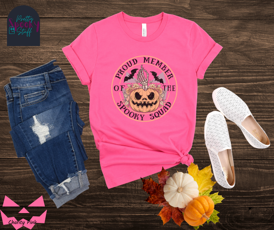 Pumpkin Halloween shirt with jack o' lantern in front of sunflowers, a skeleton hand popping out the top, two bats above, and the words "proud member of the spooky squad" making a circle around it all, faded vintage look, in charity pink.