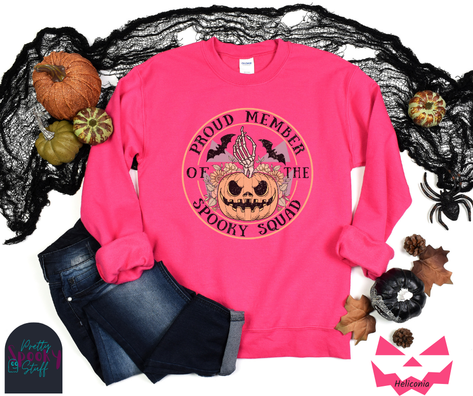 Halloween sweatshirt with a skeleton hand coming out of a jack o lantern with flowers behind it, two bats above it, surrounded by the words "proud member of the spooky squad" in a circle, in heliconia.