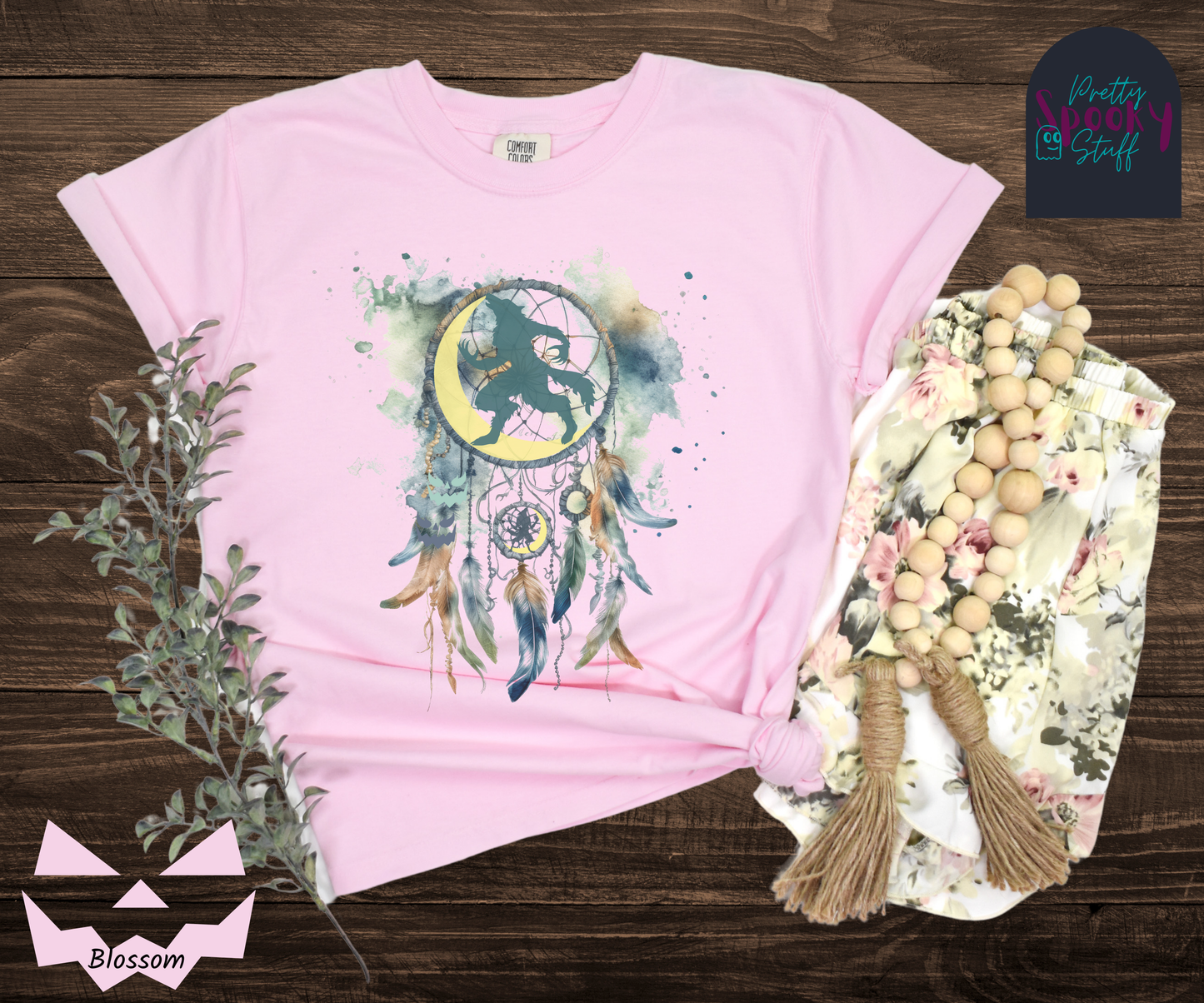 Halloween werewolf dreamcatcher shirt, watercolor aesthetic in blues and browns, featuring teal howling werewolf silhouette with yellow crescent moon in the main circle, with another werewolf/moon and jack o' lantern hiding amongst the several feathers and small circle hanging below, in blossom.