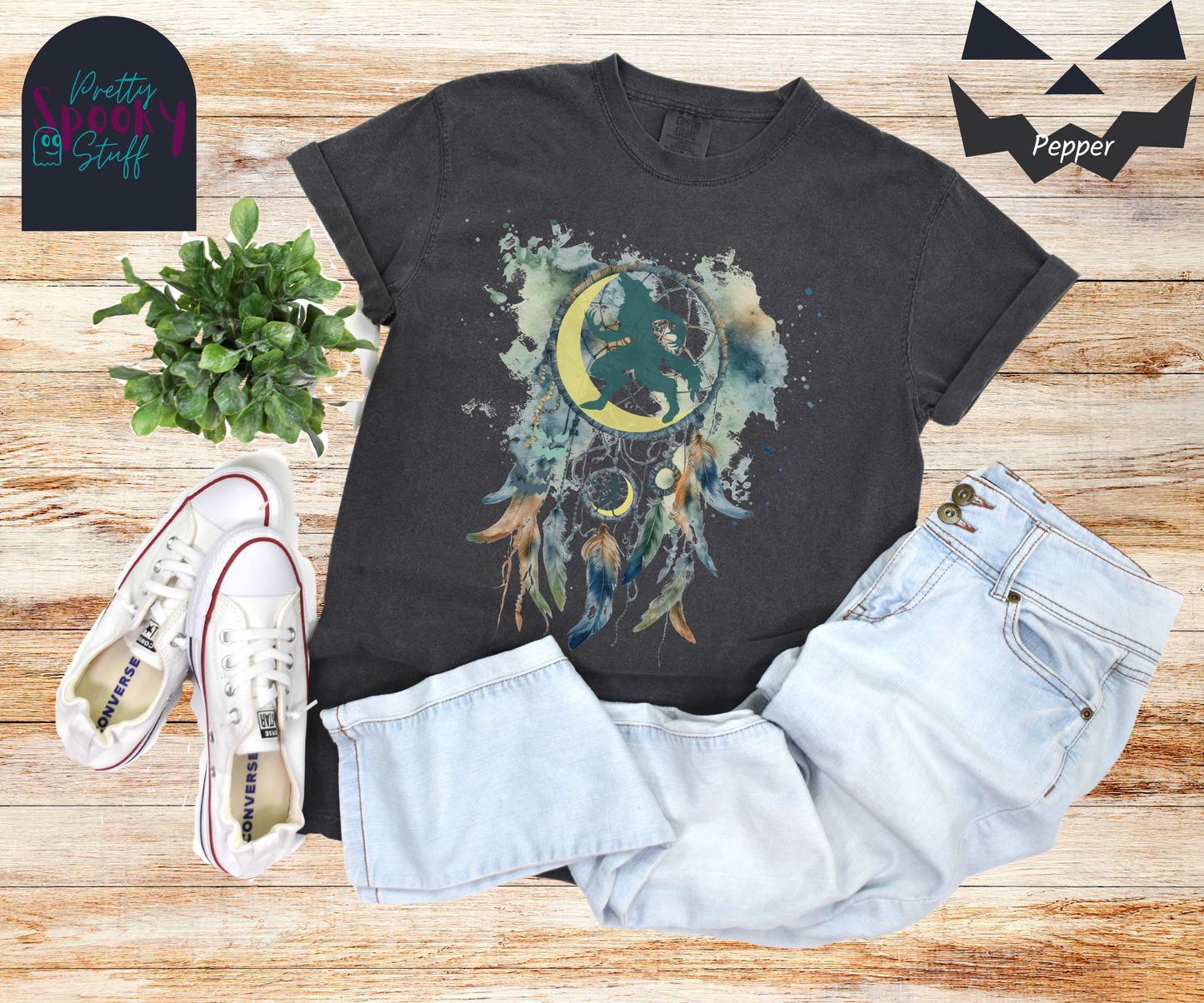 Halloween werewolf dreamcatcher shirt, watercolor aesthetic in blues and browns, featuring teal howling werewolf silhouette with yellow crescent moon in the main circle, with another werewolf/moon and jack o' lantern hiding amongst the several feathers and small circle hanging below, in pepper.