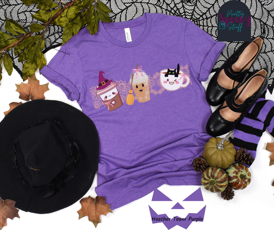 Coquette Halloween shirt with three different coffee cups, a to-go cup wearing a purple witch hat, an iced coffee with a witch broom, and a white mug with black cat hanging on the ledge from the inside, and light pink lace behind them, in heather team purple.