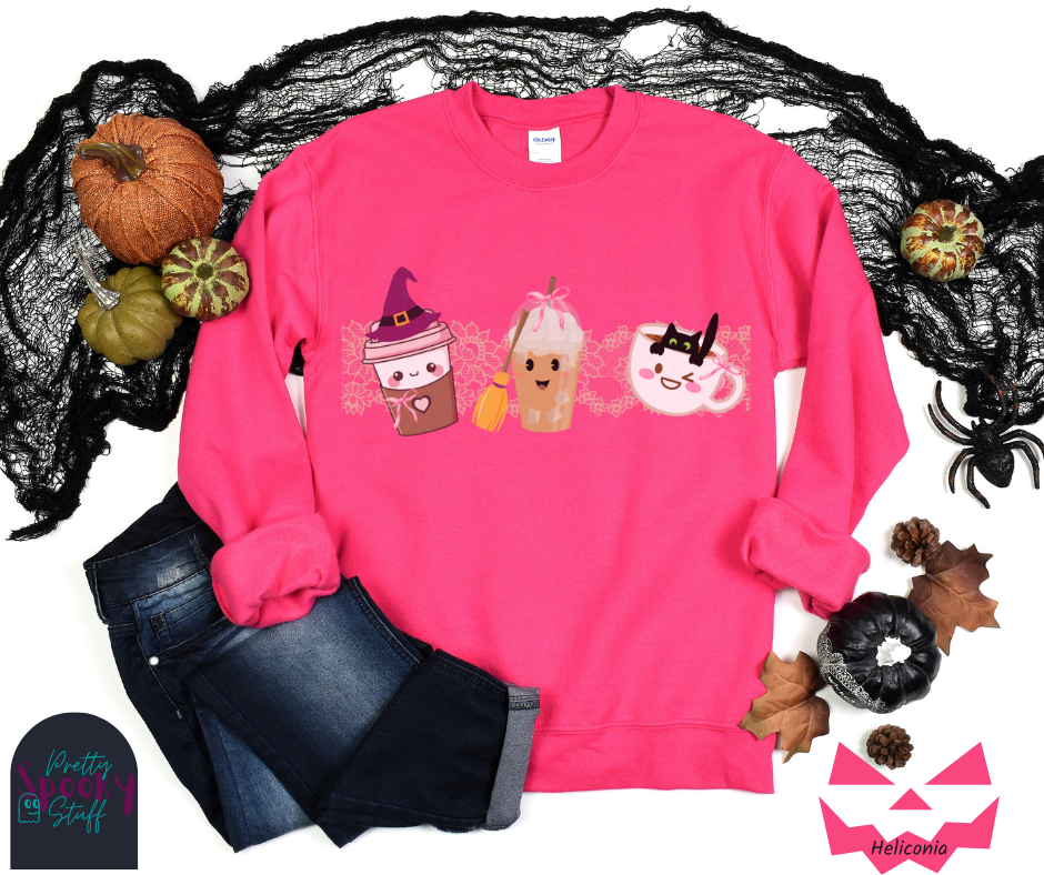Coquette Halloween sweatshirt with to-go coffee cup character wearing a witch hat and pink bow, an iced coffee cup character with a witch broom and pink bow, and a white coffee mug character with a black cat hanging on to the edge from the inside, with strip of pink intricate lace behind them all, in heliconia.