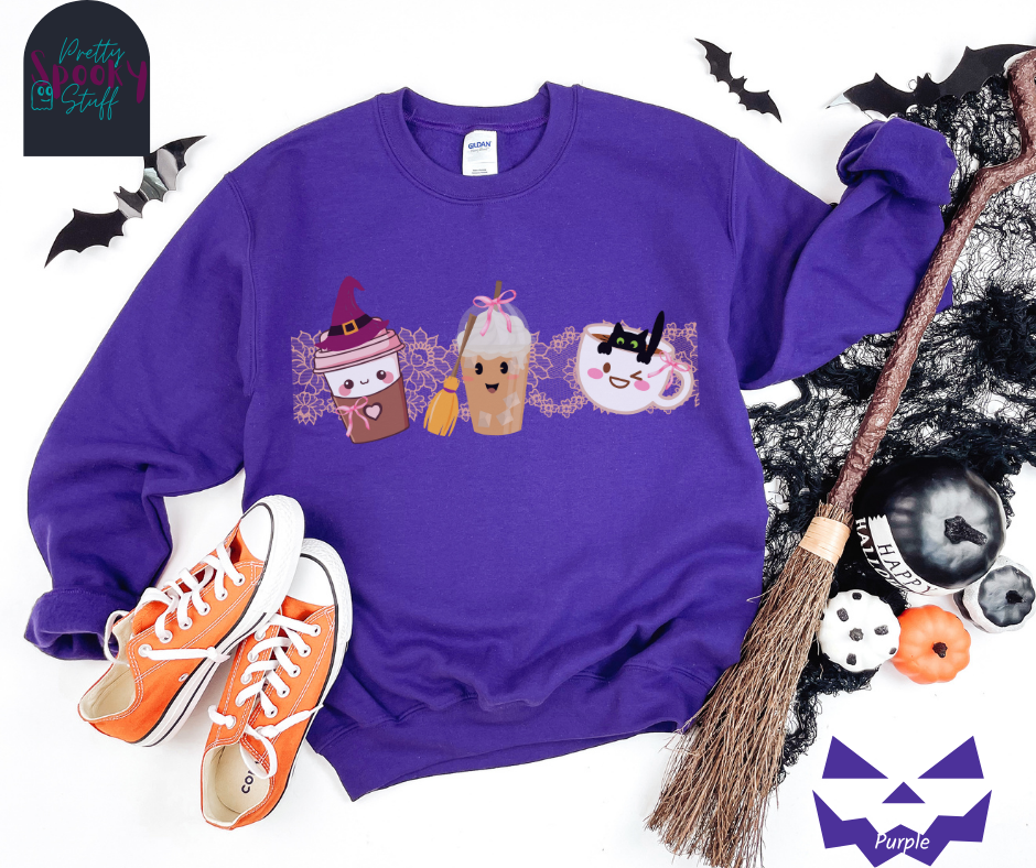 Coquette Halloween sweatshirt with to-go coffee cup character wearing a witch hat and pink bow, an iced coffee cup character with a witch broom and pink bow, and a white coffee mug character with a black cat hanging on to the edge from the inside, with strip of pink intricate lace behind them all, in purple.