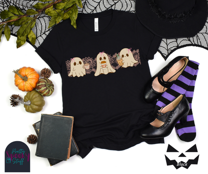 Coquette Halloween shirt with three adorable ghosts, each enjoying their own coffee beverage, adorned with a pink bow, with light pink intricate lace design behind them, in black.