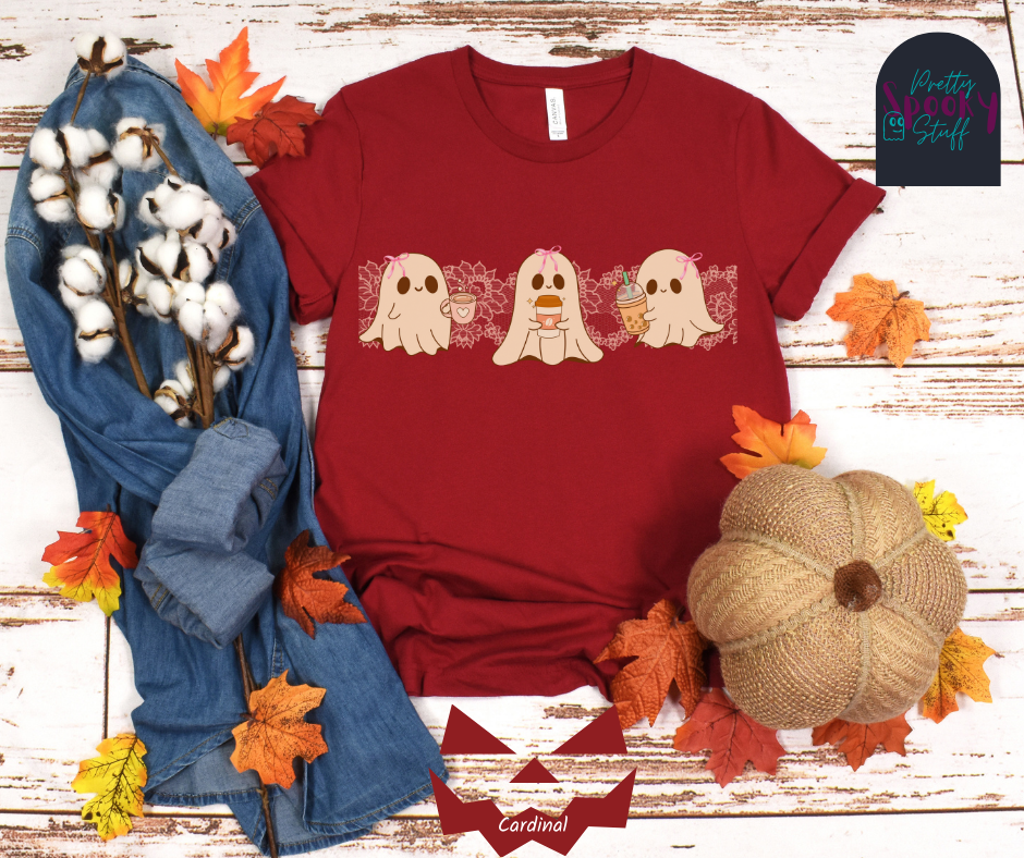 Coquette Halloween shirt with three adorable ghosts, each enjoying their own coffee beverage, adorned with a pink bow, with light pink intricate lace design behind them, in cardinal.