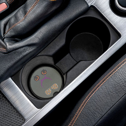 Halloween car coaster with pair of aviator glasses filled with ghosts and pumpkins in the lenses, topped with a purple headband donning dark colored jack o' lanterns, gray background, shown in car cup holder.
