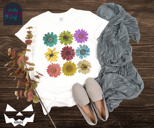 Spooky Girl Summer softstyle tee, featuring 9 colorful daisies with three black widow spiders, and one web sitting on top of them, in white. 