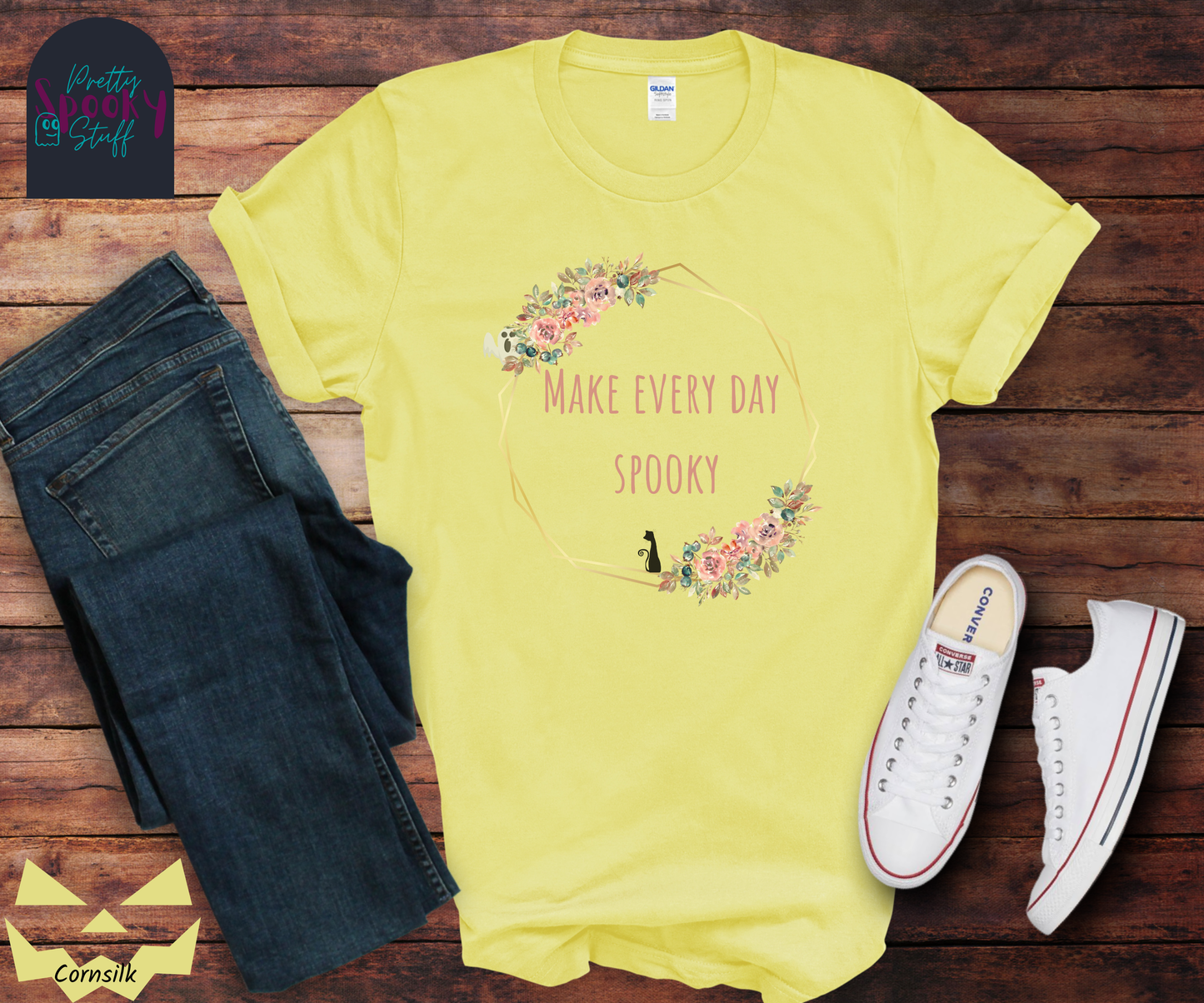Typography shirt with the words "make every day spooky" in the middle of a gold circular frame with floral details and a black cat sitting on the bottom and a ghost peaking from the top, in cornsilk.