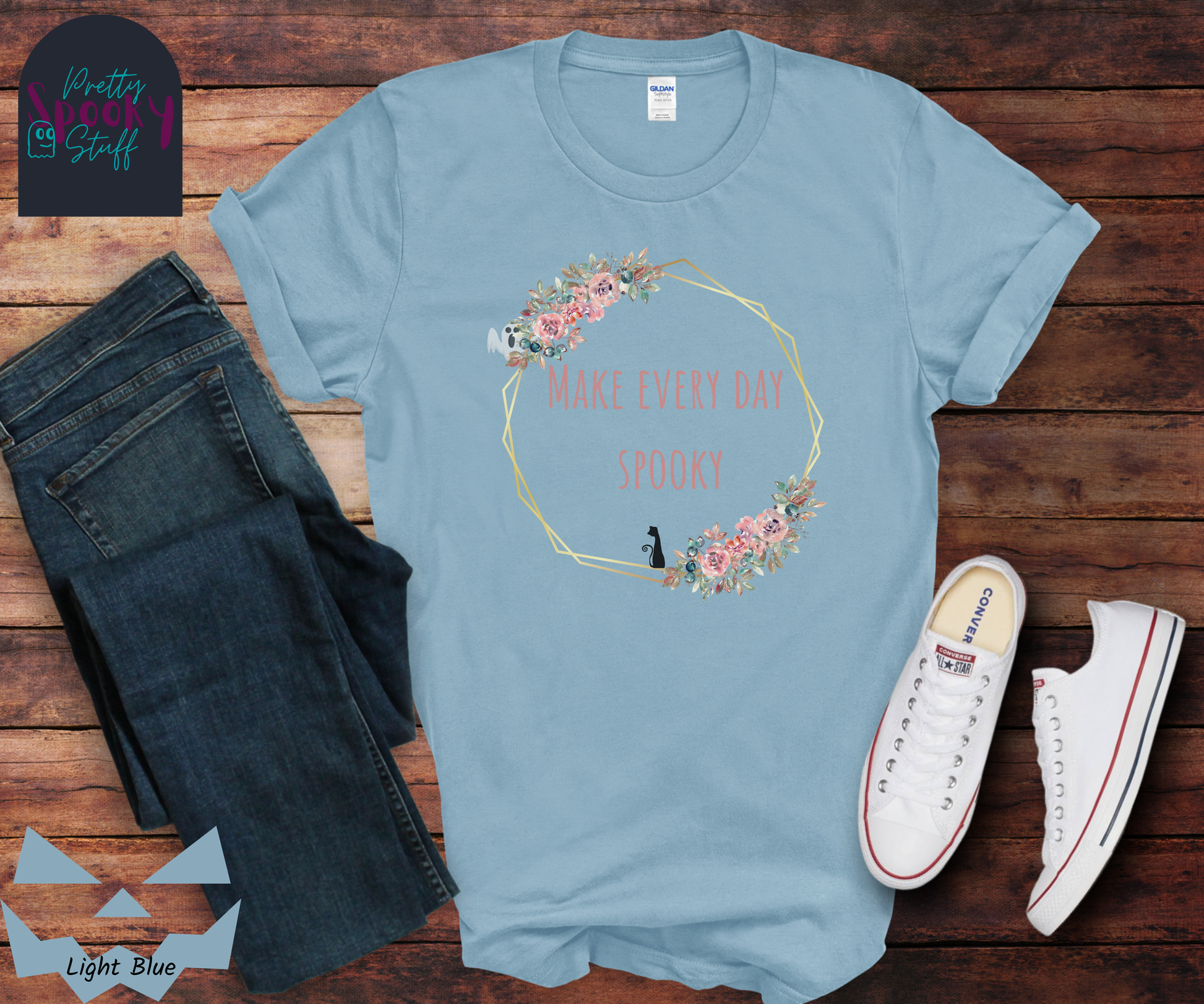Typography shirt with the words "make every day spooky" in the middle of a gold circular frame with floral details and a black cat sitting on the bottom and a ghost peaking from the top, in light blue.