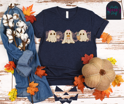 Coquette Halloween shirt with three adorable ghosts, each enjoying their own coffee beverage, adorned with a pink bow, with light pink intricate lace design behind them, in heather navy.